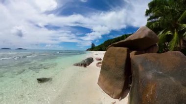 Turkuaz su ve tropikal yeşillik içeren beyaz kumlu bir sahilde büyük, aşınmış granit kayalar. Seyşeller, La Digue.