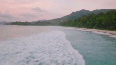 Yumuşak dalgalar, yoğun yeşil yapraklarla çevrili, kumlu bir tropikal plaja yuvarlanıyor. Büyük Anse. Seyşeller, Mahe.