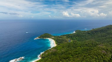 Turkuaz sular, yeşil tepeler ve parçalı bulutlu gökyüzünün altındaki ormanlık alanlarla çevrili geniş bir körfez etrafında kıvrılır. Seyşeller, Mahe.