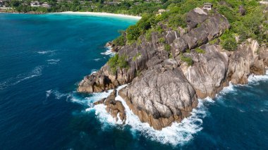 Turkuaz suları olan kayalık bir kıyı şeridi ve yeşilliklerle çevrili kayalara çarpan dalgalar. Seyşeller, Mahe.