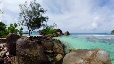 Mavi gökyüzünün altında turkuaz okyanus suyu ve yemyeşil tropik yemyeşil manzaralı kayalık kıyı şeridi. Seyşeller, Mahe. Port Glaud Gölü.