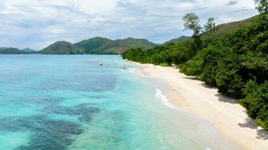 Bereketli yeşil ağaçlar ve kayan tepelerle çerçevelenmiş turkuaz suları olan güzel, beyaz kumlu bir sahil. Praslin, Seyşeller.