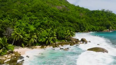 Kıyı şeridi yemyeşil bitki örtüsü ve kıyıya vuran turkuaz dalgalarla kaplı. Seyşeller, Mahe.