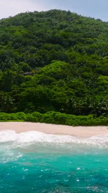 Kumlu bir sahil, yoğun yeşil tepeler ve bitki örtüsüyle çerçevelenmiş turkuaz sularla karşılaşıyor. Anse Boileau. Seyşeller, Mahe.
