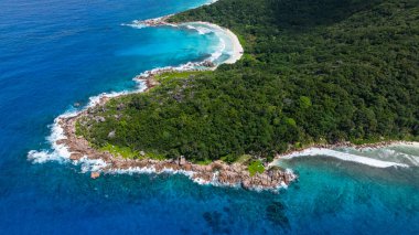 Turkuaz okyanus suları, kayalık çıkıntıları ve kumlu plajları olan yemyeşil bir sahil şeridiyle karşılaşıyor. La Digue, Seyşeller.