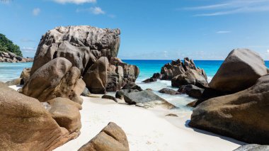 Açık mavi gökyüzünün altında turkuaz okyanusla kumsalda granit kayalar. Anse Patates, Seyşeller.