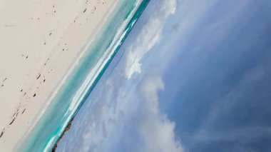 Turkuaz dalgalar, parlak bir gökyüzünün altında beyaz kumlu kıyıya çarpıyor. Uzakta kayalık oluşumlar var. Seyşeller, La Digue. Anse Komandoları.