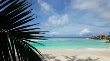 Açık mavi dalgalar parlak bir gökyüzünün altında beyaz bir kumsalda kıyıya vurur. Seyşeller, La Digue. Anse Komandoları.