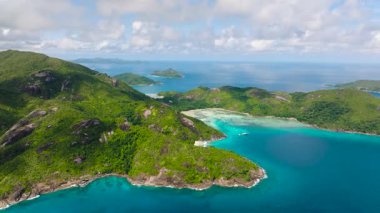 Ufuktaki uzak adalarla benekli turkuaz sulara uzanan yeşil tepeli kıyı şeridi. Seyşeller, Mahe.