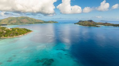 İki tropikal ada, kristal berrak turkuaz sularla çevrili sakin bir körfez boyunca karşı karşıya. Praslin, Seyşeller.