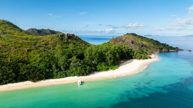Yeşil yemyeşil tepeler ve kayalık kayalıklarla çevrili kristal berraklığında turkuaz suyu olan uzak bir sahil. Curieuse, Seyşeller.