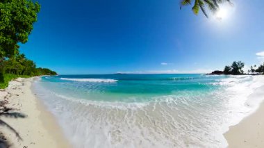 Yumuşak turkuaz dalgalar, temiz mavi gökyüzü ve ufuktaki uzak adalarla el değmemiş beyaz kumsala vurur. Seyşeller, Praslin. Constance Lemuria Sahili.
