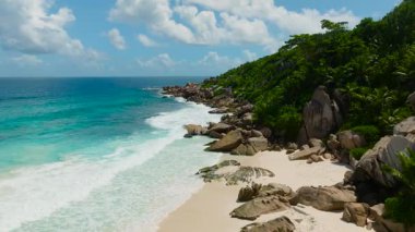 Kıyı şeridi, açık bir gökyüzünün altında mavi dalgalar kıyıya çarpıyor. La Digue, Seyşeller.