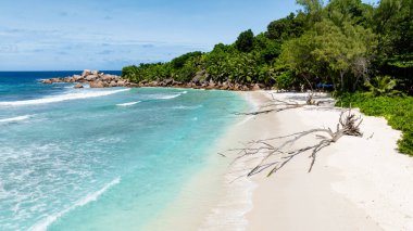 Kıyı şeridi boyunca yeşil ormanlı beyaz kumsalda ayak izleri. Anse Cocos Plajı, Seyşeller.