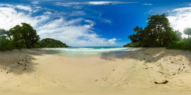 Yumuşak dalgalar, hareketli bir gökyüzünün altında yoğun tropikal ağaçlarla kaplı sakin ve kumlu bir kıyıya rastlar. Anse Louis plajı, Seyşeller. 360 görünüm.