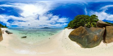 Kristal gibi berrak sığ suları, pürüzsüz kayaları ve gür tropikal bitki örtüsüyle canlı mavi gökyüzüne karşı kurulmuş sakin bir sahil. Anse Gaulettes. La Digue, Seyşeller. VR 360.