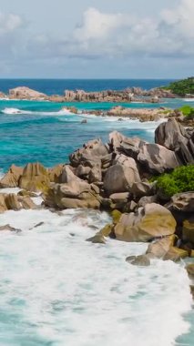 Kıyı şeridi boyunca yemyeşil ve turkuaz dalgalarla çevrili granit kayalar. La Digue, Seyşeller.