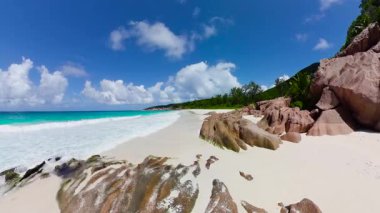 Parlak mavi gökyüzünün altında pürüzsüz granit kayalar ve turkuaz okyanusla beyaz kumsal. Seyşeller, La Digue. Küçük Anse.