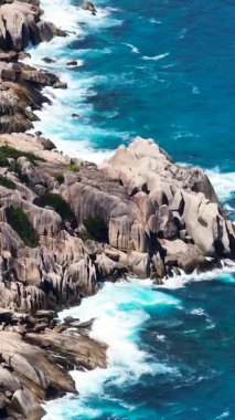 Büyük granit kaya oluşumları, dalgaların mavi okyanusta onlara çarpmasıyla kıyı şeridini oluşturur. Seyşeller, Felicite.