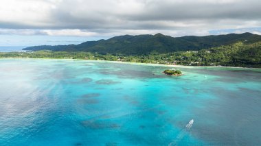 Canlı turkuaz suların havadan görünüşü yemyeşil bir sahil şeridinin yakınındaki yemyeşil, küçük bir adayı çevrelemektedir. Praslin, Seyşeller.