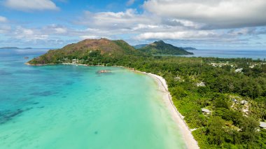 Yeşil tepeleri, sakin bir turkuaz körfezi ve yumuşak beyaz kumları olan kavisli bir sahil şeridi. Praslin, Seyşeller.