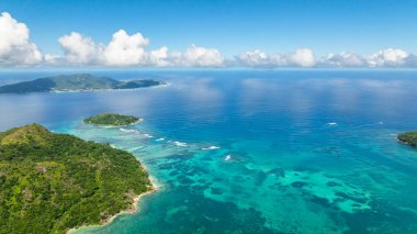 Berrak turkuaz okyanusla çevrili yemyeşil adalar beyaz bulutlu açık mavi bir gökyüzünün altında. Seyşeller, Mahe.