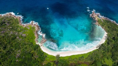 Sarp kayalıklarla çevrili turkuaz körfez ve sakin plajlı yoğun yeşil bitki örtüsü. Anse Cocos plajı. La Digue, Seyşeller.