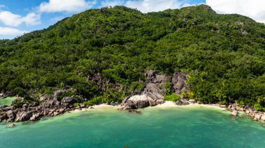 Sahil şeridi boyunca berrak turkuaz sular, büyük kayalar ve yoğun bitki örtüsünün yer aldığı çarpıcı bir sahil manzarası. Praslin, Seyşeller.
