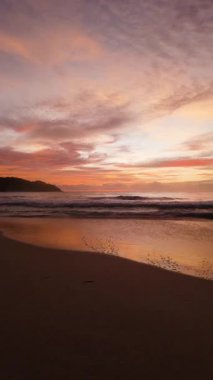 Gün batımının canlı renkleri, yumuşak dalgalar kıyıya değdiğinde, pembe ve turuncu gölgeli bir gökyüzünün altında ıslak kuma yansıyor. Seyşeller, Praslin.