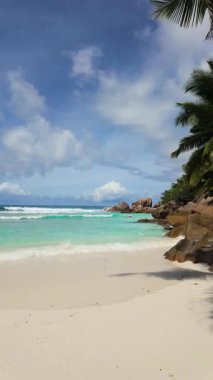 Turkuaz dalgalar büyük granit kayalar ve gür palmiye ağaçları ile çevrili beyaz kumlu kıyıya nazikçe ulaşır. Seyşeller, La Digue.