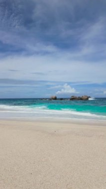 Geniş, kumlu bir sahil, kabarık bulutlarla dolu bir gökyüzünün altında berrak mavi sularla uzanır. Anse Boileau. Seyşeller, Mahe.