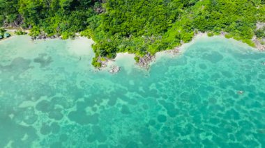 Berrak turkuaz suların havadan görünüşü kayalık çıkıntılı yemyeşil bir kıyı şeridine nazikçe yaklaşıyor. Praslin, Seyşeller.