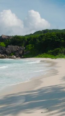 Üzerinde turkuaz dalgaların dolaştığı kumlu sahil şeridi ayak izleri ve yemyeşil alanlar gösteriyor. La Digue, Seyşeller. Grand Anse Sahili.