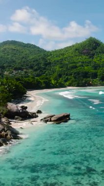 Geniş turkuaz sular, kıyıdan gelen yumuşak dalgalarla yemyeşil bir kıyı şeridiyle karşılaşır. Baie Lazare. Seyşeller, Mahe.