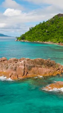 Yeşil bir yamacın yakınındaki sakin zümrüt sulardan yükselen engebeli kayaların olduğu sakin bir sahil manzarası. Praslin, Seyşeller.