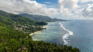 Turkuaz okyanus suyu yoğun bir orman kıyı şeridiyle sınırlıdır, mercan resifleriyle kristal berraklığında. Seyşeller, Mahe.