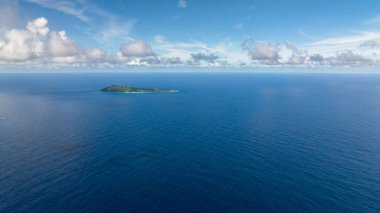 Uçsuz bucaksız, sakin, mavi bir okyanusun ortasında uzanan küçük yeşil ada dağınık bulutlarla dolu parlak bir gökyüzünün altında. Seyşeller, La Digue.