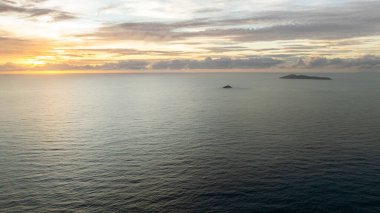 Sakin sular ufuk çizgisine, uzakta küçük bir adayla, yumuşak bir günbatımı parıltısının altında ulaşır. Seyşeller.