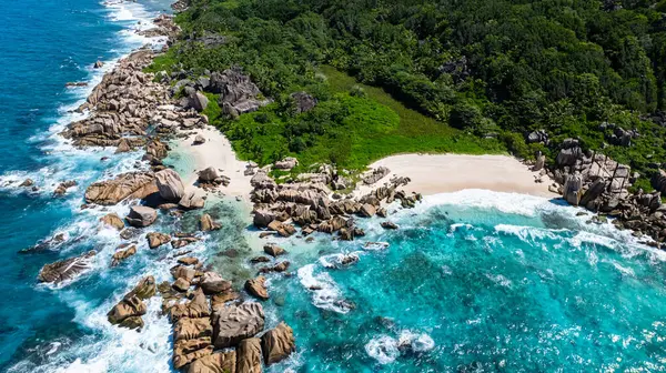 Dalgalar, kıyı boyunca turkuaz sularla çevrili engebeli granit kayalara çarpıyor. La Digue, Seyşeller. Anse Marron Sahili.