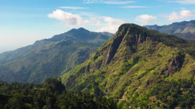 Mavi gökyüzü ve bulutlardan oluşan bir arka planda ormanla kaplı dağların üst manzarası. Sri Lanka 'daki dağlık arazi.