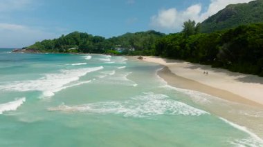 Sahil şeridi boyunca yumuşak sörf ve canlı tropikal yapraklarla dolu. Seyşeller, Mahe. Grand Anse Sahili.