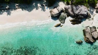 Yeşil yapraklarla çevrili, tropik bir plajın turkuaz suyu ile büyük kaya oluşumları. Seyşeller, Mahe. Roche Copra.