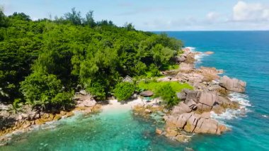 Büyük kayalar, yemyeşil bitki örtüsü ve okyanusla buluşan turkuaz suyla kıyı manzarası. Seyşeller, La Digue. Timsah Sahili.