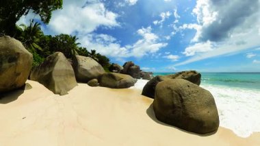 Büyük granit kayaları ve yemyeşil bitki örtüsü olan beyaz kumsal. Seyşeller, La Digue.