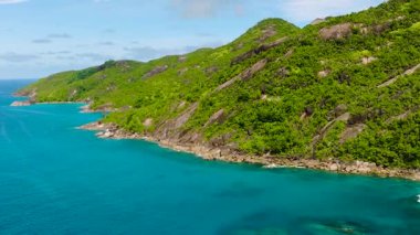 Mavi gökyüzünün altında kristal berrak turkuaz sulara inen yeşil dağlık kıyı şeridi. Seyşeller, Mahe. Victoria..