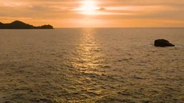 Altın günbatımı ışığı okyanus dalgalarını yansıtır kaya oluşumları ve uzak kara ile, huzurlu bir manzara yaratır. Seyşeller, Mahe.