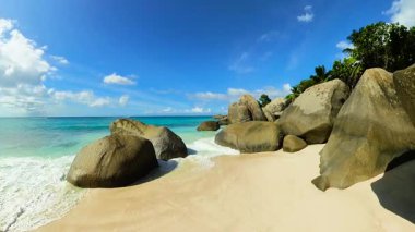 Büyük granit kayaları ve parlak mavi gökyüzünün altında berrak okyanus suyu olan tropik bir sahil. Seyşeller, La Digue.