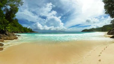 Turkuaz okyanus dalgaları, yoğun tropikal bitki örtüsüyle çevrili el değmemiş kumlu bir plaja yuvarlanıyor. Seyşeller, Mahe. Anse Niyet.