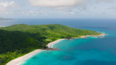 Turkuaz bir okyanus ve beyaz kumlu plajla buluşmak için eğimli yemyeşil tepelerin havadan görünüşü. Seyşeller, La Digue.