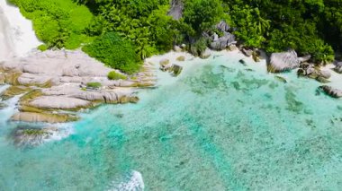 Granit oluşumlar, yeşilliklerle çevrili beyaz kumlu bir sahil boyunca berrak turkuaz sularla buluşur. Seyşeller, La Digue.